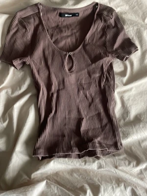Ribbad brun topp från Bik Bok - Säljer en ribbad brun topp från Bik Bok i storlek XS. Toppen har korta ärmar, rundad v-ringning med liten knappdetalj framtill och är i stretchigt material. Perfekt att styla med jeans eller kjol.
