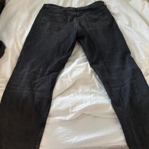Svarta raka jeans från Lee - Säljer ett par svarta jeans från Lee med rak passform och klassiska fem fickor. Jeansen har en diskret tvättad look och är tillverkade i denim med en mjuk känsla. Perfekta för dig som gillar en enkel och stilren stil. 33/32
