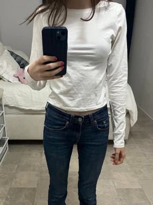 Vit långärmad topp i bomull - En enkel och stilren vit långärmad topp med rund halsringning. Tillverkad i mjuk bomull och har en normal passform som sitter snyggt på kroppen. Perfekt att matcha med jeans eller kjol för en clean look.