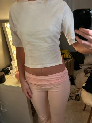 Vit croppad topp från Nelly - Säljer en kroppad T-shirt med lite öppen rygg o rosätt där bak. Skit snygg passar till allt säljer då jag inte använt den och kommer säkert inte göra. 