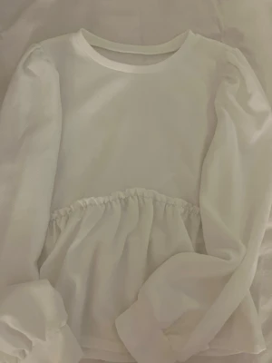 Vit långärmad topp från SHEIN 💞 - Söt vit långärmad topp från SHEIN med rund halsringning och volangdetalj i midjan. Tillverkad i mjuk polyesterblandning som känns skön mot huden. Perfekt för dig som gillar en enkel men ändå trendig look.💞