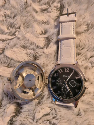 Vit Geneva klocka med 50 Cent-lock - Unik klocka från Geneva med vitt armband  50 cent loggan går att snurra på och glittriga detaljer. Klockans urtavla är svart med silver siffror och flera dekorativa småurtavlor. Perfekt för dig som vill sticka ut!