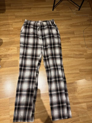 Rutiga pyjamasbyxor - Mysiga pyjamasbyxor i brun, vitt och grått rutmönster. Byxorna har rak passform, resår i midjan. 