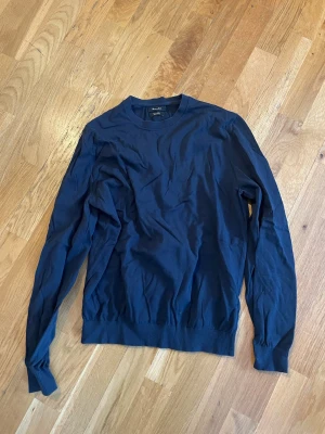 Mörkblå rundhalsad tröja - En stilren mörkblå tröja, rund halsringning och långa ärmar. Tillverkad i mjukt bomullsmaterial och har ribbade muddar vid ärmslut och nederkant. Perfekt för en enkel och clean look.