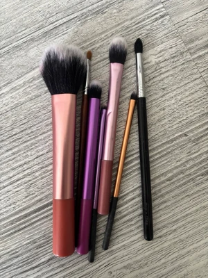 Set med sminkborstar i olika färger - Säljer ett set med sex sminkborstar från Real Techniques och Sigma. Borstarna har handtag i rosa, lila, svart och koppar, och borsthåren är mjuka i svart och vitt. Perfekta för både puder, ögonskugga och detaljer. Materialet är syntetiska fibrer och metall.