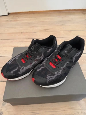 Svarta Reebok sneakers - Snygga svarta sneakers från Reebok med grått camomönster och röda detaljer på snörningen. Skorna har en låg profil och vit sula. 