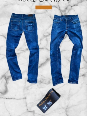 Nudie Jeans - Grim Tim - Säljer ett par blå skinny jeans från Nudie Jeans med klassisk femficksdesign och kontrastsömmar. Jeansen har en smal passform och är tillverkade i stretchigt denimtyg för extra komfort. Perfekta för dig som gillar en clean och tidlös look.