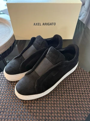 Svarta Axel Arigatos - Stilrena svarta sneakers från Axel Arigato i mocka. Skorna är i riktigt bra skick 10/10 använt kanske max 4 gånger på sommaren köpta 2025, säljer på grund av att dom är för små för mig. Äktehets bevis finns, du får med allt OG också! Så som box och dustbag. Ny pris 2600kr