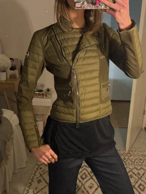 Olivgrön pufferjacka från Colmar - Snygg olivgrön pufferjacka från Colmar med asymmetrisk dragkedja, hög krage och quiltade partier. Jackan har två framfickor med tryckknappar och dragkedja samt Colmar-logga på ärmen. Perfekt för kalla dagar och ger en cool, sportig look.