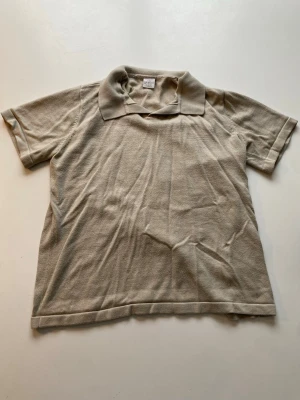 Beige piké t-shirt med krage - En enkel beige piké t-shirt med klassisk krage och korta ärmar. Tillverkad i mjuk bomull som känns skön mot huden. Perfekt för en avslappnad och stilren look. Passformen är normal och färgen är diskret beige. 