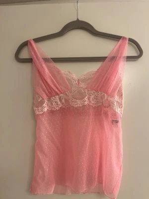 Rosa spetsnattlinne med mesh - Sött rosa linne i transparent mesh med tunna axelband och vacker spets upptill. Perfekt för lager-på-lager eller som statement-piece.