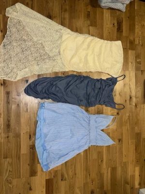 Tre klänningar i spets och pastell - Säljer tre klänningar: en lång gulfärgad spetsklänning med omlott och transparent nederdel, en mörkblå tight klänning med smala axelband samt en ljusblå kort klänning med v-ringning och volangkant. Perfekta för sommarens alla tillfällen!