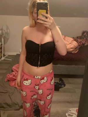 Svart korsett topp från h&m - Säljer en svart bandeau topp med nitar framtill. Toppen är axelbandslös och har en croppad passform. Perfekt för dig som gillar en edgy och trendig stil. Materialet känns mjukt och stretchigt. 