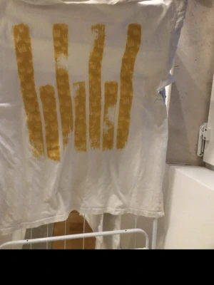 Vit Rave Culture t-shirt med tryck - Vit t-shirt från Rave Culture med unikt guld tryck framtill och texten 'Rave Culture' på baksidan. T-shirten har korta ärmar och är gjord i mjuk bomull, perfekt för dig som gillar streetwear och vill sticka ut. Går inte att få tag i denna modellen längre. Jag vill ha 450kr för den.