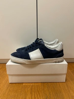 Valentino flycrew - Snygga flycrews från Valentino i marinblå mocka med vita detaljer och vit sula. Klassisk låg modell med blå skosnören och diskret logga på plösen. Skorna är lite slitna där bak och har tappat några nitar men det märks inte vid användning och är minst lika snygga. Tveka inte med att fråga. Priset är ej hugget i sten.