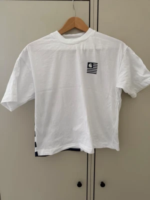Vit Carhartt t-shirt med tryck - Säljer en vit t-shirt från Carhartt med coolt grafiskt tryck i rött och marinblått på ryggen och liten logga fram. T-shirten har korta ärmar och är gjord i mjuk bomull. Perfekt för dig som gillar streetwear och vill sticka ut lite extra.