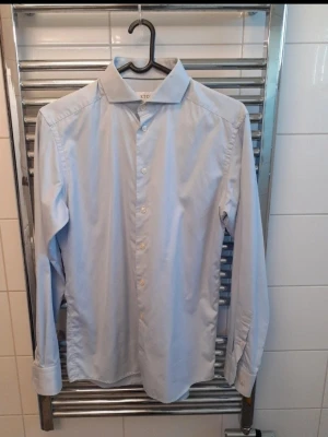 Ljusblå skjorta från Eton - Klassisk ljusblå skjorta från Eton med lång ärm och knappar framtill. Skjortan har en stilren krage och är tillverkad i mjuk bomull som känns skön mot huden. Perfekt för dig som gillar en clean och tidlös look. Slimfit model.