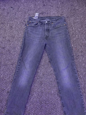 Levi's raka ljusgrå jeans - Klassiska grå jeans från Levi's med rak passform och fem fickor. Jeansen har en vintage tvätt och tydliga sömmar, samt den ikoniska läderpatchen bak i midjan. Perfekta för en avslappnad och tidlös stil.