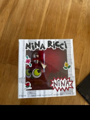 Nina Ricci Nina Limited Edition parfym - Unik limited edition parfym från Nina Ricci i en cool röd äppelformad flaska med stora tecknade ögon och en fluffig röd boll på korken. Flaskan rymmer 50 ml och har en lekfull design med färgglada detaljer och blommor på förpackningen.