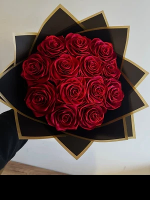 Bukett med röda konstgjorda rosor - Snygg bukett med röda konstgjorda rosor, omsorgsfullt arrangerade i svart och guldigt papper. Perfekt som dekoration eller present. Rosorna har en realistisk form och djup röd färg som verkligen sticker ut.