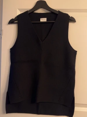 Svart stickad väst från VILA - Snygg svart stickad väst från VILA med v-ringad hals och diskreta detaljer vid sidorna. Västen har en rak passform och är perfekt att styla över en skjorta eller t-shirt för en trendig lager-på-lager-look.