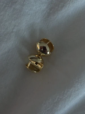 Små guldiga chunky örhängen - Stilrena örhängen i blank guldig metall med chunky, rundad form. De har en modern och minimalistisk design som ger en cool touch till din outfit. Perfekta för dig som gillar statement-smycken. Pläterade i 14 karats guldplätering. Allergivänliga och Nickelfria 💛