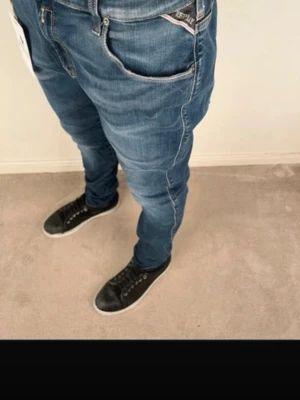Replay blå slim fit jeans - Säljer ett par blå slim fit jeans från Replay med klassisk femficksdesign och snygga kontrastsömmar. Jeansen har dragkedjegylf och Replay-logga på fickan fram samt läderpatch bak i midjan. Perfekta för en avslappnad men trendig look. Size: 32 48