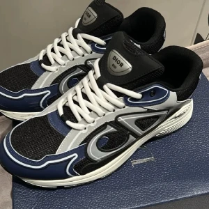 Dior B30 sneakers blå,svart och grå - Snygga Dior B30 sneakers i blått, svart och vitt med stora reflekterande detaljer på sidorna och vit sula. Ovandelen är i mesh och läder, med vita skosnören och tydlig Dior-logga. Perfekta för dig som gillar exklusiva och trendiga sneakers. De är använda 2 gånger! Skriv om ni har några frågor