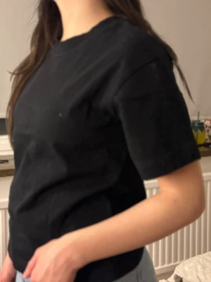 Svart basic t-shirt i bomull - En enkel svart t-shirt med rund hals och korta ärmar. Modellen är rak och klassisk, perfekt till jeans eller shorts. Tillverkad i mjuk bomull för en skön känsla. Inga synliga tryck eller loggor för en clean look.