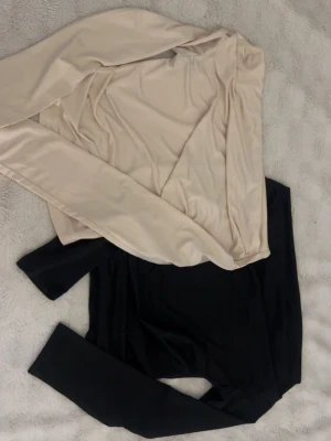 Två långärmade offshoulder toppar i svart och beige - Säljer två stilrena långärmade toppar i svart och beige. Båda är i mjukt, stretchigt material med figurnära passform och rund halsringning. Perfekta att matcha med jeans eller kjol för en enkel och snygg look.