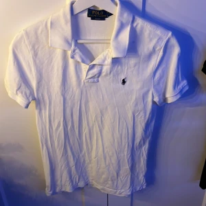 Vit kortärmad pikétröja från Ralph Lauren - Säljer en klassisk vit pikétröja från Ralph Lauren i slim fit. Tröjan har en broderad logotyp på bröstet och korta ärmar. Perfekt för en stilren look.