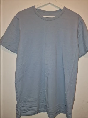 Ljusblå t-shirt i bomull - Enkel och stilren ljusblå t-shirt. Perfekt för en avslappnad look och lätt att matcha med andra plagg. Tillverkad i mjuk bomull för skön komfort.
