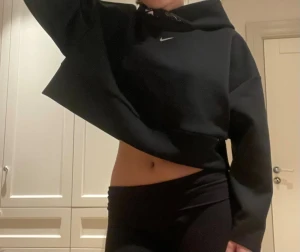 Svart cropped hoodie från Nike - Säljer en svart cropped hoodie från Nike med liten vit logga på bröstet och tryck på insidan av huvan. Hoodien har oversized passform, långa ärmar och är gjord i mjukt sweatshirtmaterial. Perfekt för en sportig och avslappnad stil.