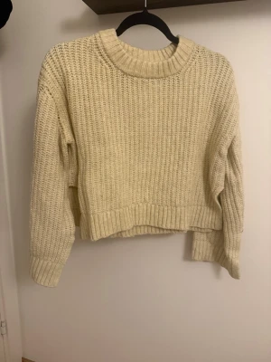 Ljusgul croppad stickad tröja - Säljer en ljusgul croppad stickad tröja med grov ribbstickning och rund hals. Tröjan har långa ärmar och breda muddar vid ärmslut och nederkant. Perfekt för lager på lager och en chill look.