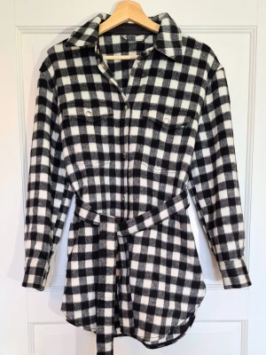 & Other Stories Checkered Belted Shacket – Paris Atelier med Rafanelli-tyg - Den här underbara shacket/kappan från & Other Stories – Paris Atelier förtjänar den en ny ägare som faktiskt använder den! Materialet är av fin kvalitet med ullblandning (45% ull) och italienskt tyg från Rafanelli. Storlek: EU 34 (passar även 36 beroende på önskad passform). Nypris 1500 kr så detta är ett jäkla kap!  Skick: I princip som ny – använd 1 gång. Lite ytludd finns men det gör det alltid med ull.