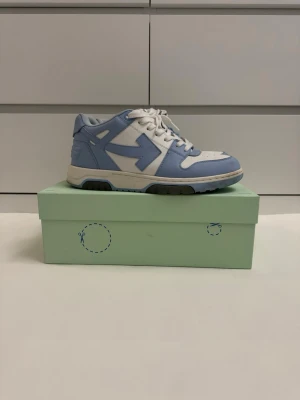 Off-White Out Of Office sneakers blå/vit - Snygga Off-White Out Of Office sneakers i vitt och ljusblått läder med Off-Whites ikoniska pil-logga på sidan. Skorna har vita snören, perforerad tå och en chunky sula. Perfekta för dig som vill sticka ut med en modern streetwear-look.