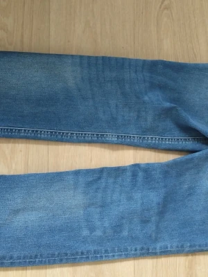 Blå raka jeans i denim - Säljer ett par klassiska blå jeans i rak modell. Jeansen är i mjuk denim med snygga slitningar och kontrastsömmar. Perfekta för dig som gillar en enkel och tidlös stil. Storlek 164 (14Y).