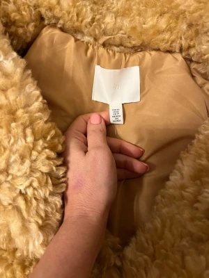 Beige teddyjacka från H&M - Supermysig teddyjacka i beige från H&M. Jackan har en fluffig och lockig yta, klassisk krage och är helfodrad med slät insida. Perfekt för dig som vill ha en trendig och varm look under kyliga dagar.