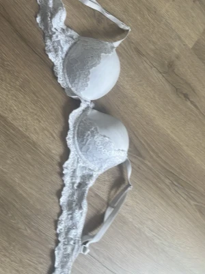 Vit spets-bh med vadderade kupor, ifrån Cubus. Storlek 65a - Snygg vit bh med vadderade kupor och fina spetsdetaljer längs kanterna. Justerbara axelband för perfekt passform. Perfekt för dig som gillar en feminin och stilren look.