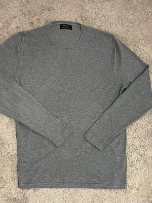 Grå långärmad tröja från Zara Man - En stilren grå långärmad tröja från Zara Man i mjukt och tunt material. Tröjan har rund halsringning och en enkel, klassisk design som passar perfekt till jeans eller chinos.