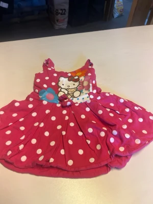 Röd prickig Hello Kitty klänning - Söt rosa kortklänning med vita prickar och Hello Kitty-tryck framtill. Klänningen har axelband och en utställd kjol. Perfekt för dig som gillar färgglada och lekfulla plagg. Materialet känns mjukt och bekvämt, troligen bomull.