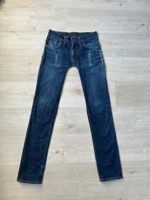 Blåa Dry Nudie Thin Finn Jeans Storlek W30 L34 - Fina Nudie Jeans i blå färg. Jeansen är i mycket bra skick och sparsamt använda. |  Äkta som allt annat jag säljer! ✅ |  Storlek: W30 L34  Skick: Mycket Bra Skick - några små slitningar men inget tydligt (SE SISTA 3 BILDER) | Färg: Blå | Märke: Nudie | Modell: Jeans |   Hör gärna av dig vid frågor så svarar jag så fort jag kan! 😁 |