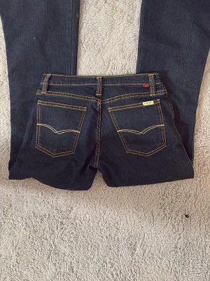Mörkblå Levi's jeans med kontrastsömmar - Snygga mörkblå jeans från Levi's med låg midja, raka ben och klassiska kontrastsömmar. Jeansen har fem fickor, bälteshällor och guldfärgade detaljer. Passar mig perfekt med storlek xs. Köpte de i en begagnad affär för 800 och använt dem två gånger. De har kanske nån liten fläck men som går säkert bort i tvätten. De är mer svart blåa än på bilden.