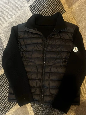 Svart dunjacka - Snygg svart dunjacka  med quiltad front och stickade ärmar. Jackan har hög krage, dragkedja framtill. Perfekt för kalla vinterdagar och riktigt trendig look. Kom privat för mer detaljde bilder svara inom 10 minuter 