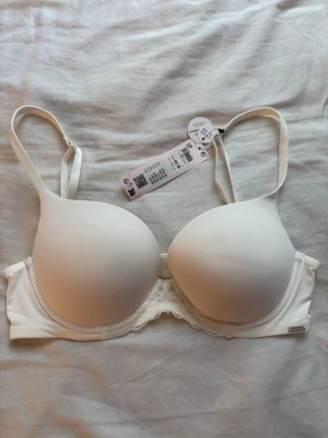 Vit push-up bh från H&M, spetsdetalj - Snygg vit push-up bh från H&M med släta kupor och justerbara axelband. Bh:n har en fin spetskant nedtill och är tillverkad i en återvunnen polyamidblandning. Perfekt för dig som vill ha en enkel men stilren bh med extra stöd.
