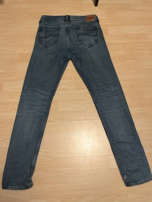 Blå raka jeans från Lee - Klassiska blå jeans från Lee med rak passform och fem fickor. Jeansen har en mellanblå tvätt och Lee-logga på bakfickan. Tillverkade i denim med snygga detaljer och normal midja. Perfekta för en avslappnad och stilren look.