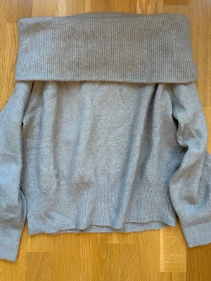 Beige-grå off shoulder stickad tröja - Säljer en beige-grå stickad tröja från H&M med bred off shoulder-krage. Tröjan har lång ärm och ribbstickade muddar vid ärmslut och nederkant. Perfekt för dig som gillar en avslappnad men trendig stil. Katt finns i hemmet, skriv om ni har frågor. 