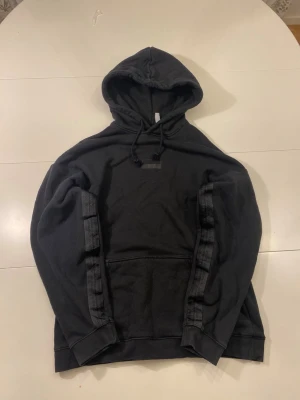 Adidas svart huvtröja, storlek S - Svart hoodie med Adidas-ränder längs ärmarna och en ficka. Observera att det finns några små hål vid fickan annars väldigt fin Hoodie. Se bild 6   Storlek: S  Längd: 64 cm Armhålsbredd: 58 cm   Ställ gärna frågor! :)