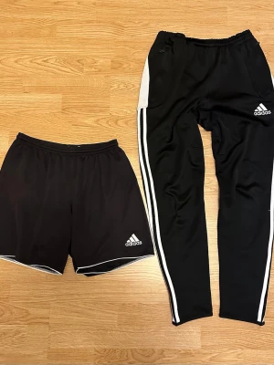 Adidas svarta träningsbyxor & shorts - Svarta träningsbyxor och shorts från Adidas med vita detaljer och logga på båda plaggen