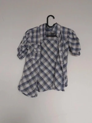 Blårutig skjorta med kort ärm - Snygg blårutig skjorta med korta ärmar och klassisk krage. Skjortan har knappar framtill och en bröstficka. Perfekt för en avslappnad stil och lätt att matcha med jeans eller shorts.